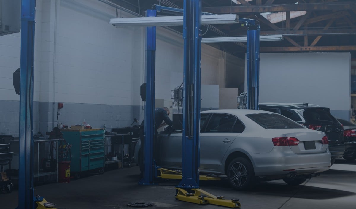An auto mechanic working on a car on a lift in a garage.