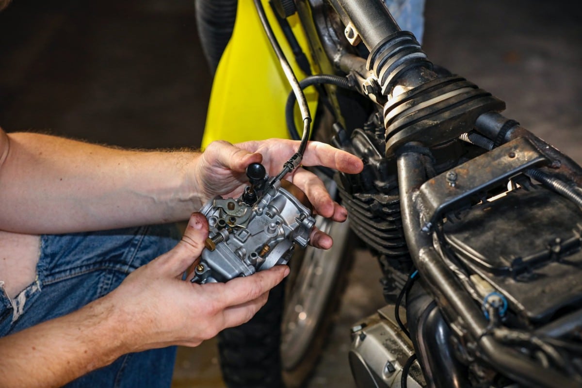 An auto mechanic is working on a motorcycle in a garage.