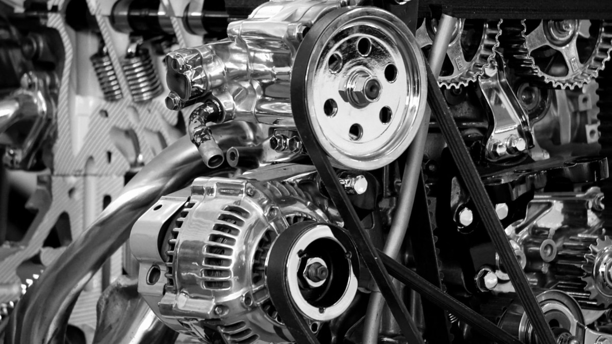 Black and white image showing detailed view of a car engine with visible gears, belts, and alternator.