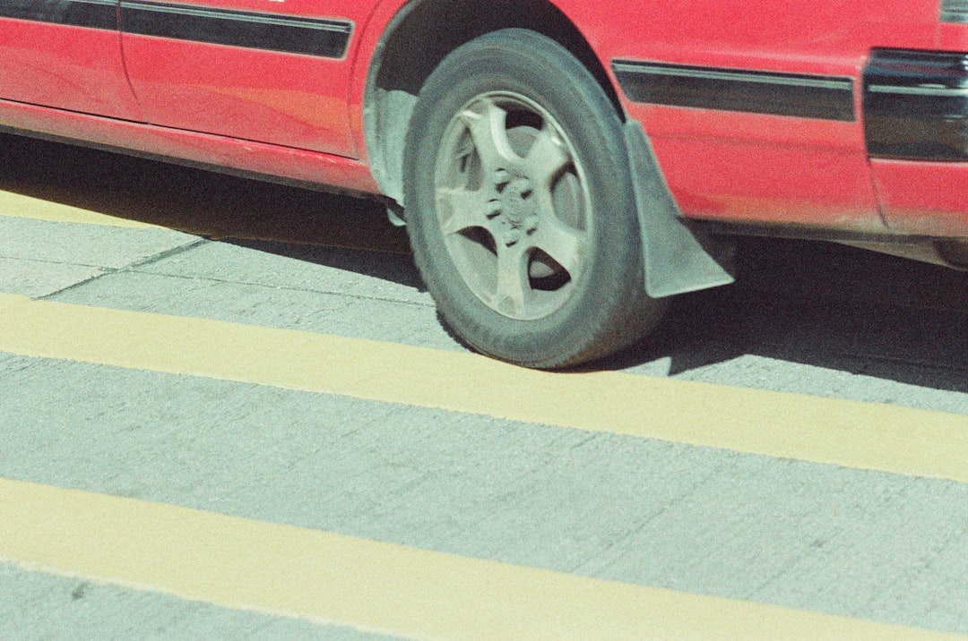 Blog | Sartorial Auto Repairs Close-up of a red car's rear wheel positioned over yellow road markings on a sunlit street, hinting at possible brake noise as the vehicle slows down.